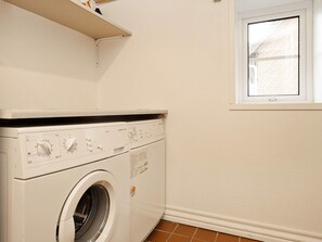 A compact laundry room with a front-loading washing machine, a small window, and a tiled floor.