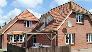 Une maison à deux étages, construite en briques, avec un toit en pente, une clôture en bois et une antenne parabolique.