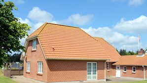 Un bâtiment en briques rouges, doté d’un toit en tuiles, d’une porte centrale et d’une petite structure adjacente.