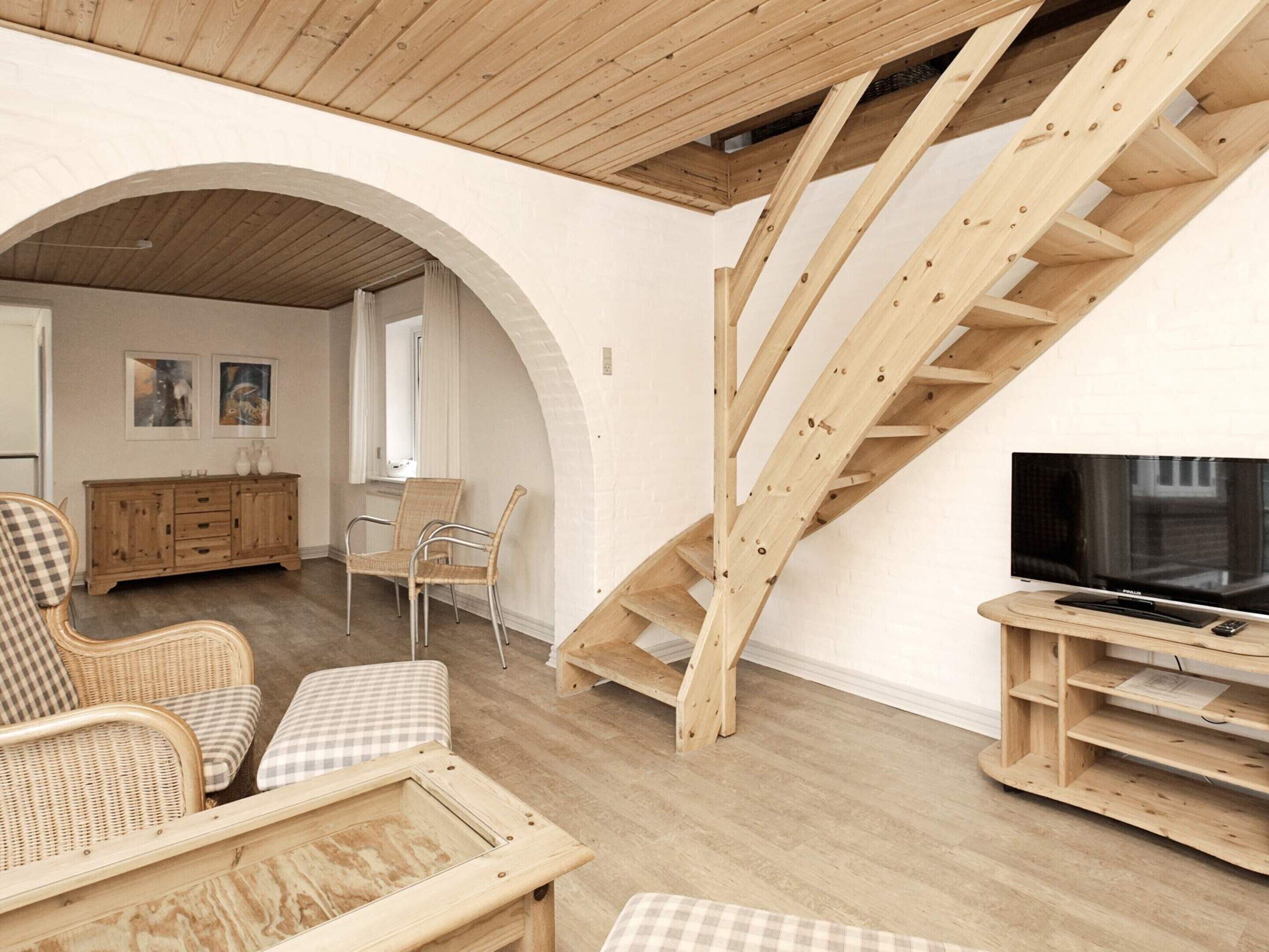A spacious living area with a wooden staircase, wicker furniture, and a flat-screen TV.