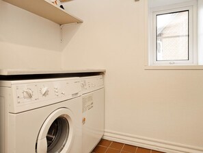 A compact laundry room with a front-loading washing machine, a small window, and a tiled floor.