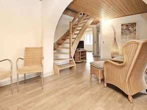 A spacious loft with a wooden staircase, wicker furniture, and a large window.