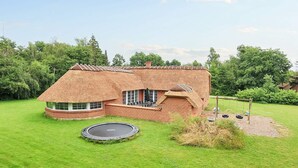 A house with a thatched roof, a brick exterior, and a trampoline in the yard. - 12 Person Holiday Home in Vaeggerlose (Vaeggerlose)