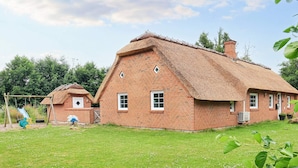 A traditional brick house with a thatched roof, a small attached shed, and a swing set in the yard. - 12 Person Holiday Home in Vaeggerlose (Vaeggerlose)