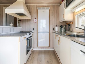 A compact kitchen with a central island, built-in oven, and a refrigerator. - 5 Star Holiday Home in Spottrup (Spøttrup)
