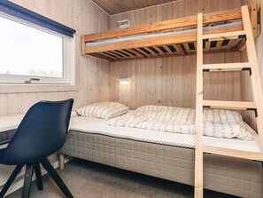 A bunk bed with a desk and chair, a window, and a wall-mounted light fixture.