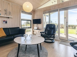 A modern living room with a black leather sofa, a round coffee table with two wine glasses, a black leather chair, a television, and a large window with a view of the outdoors. - 5 Star Holiday Home in Spottrup (Spøttrup)