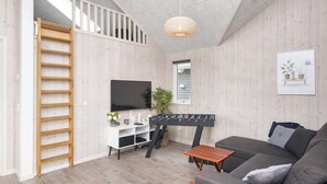Ein modernes Wohnzimmer mit grauem Sofa, Holzböden, einem Fernseher und einem Kicker.