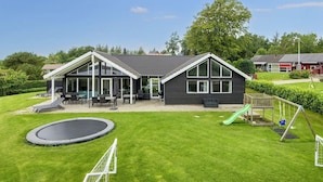 Ein modernes Haus mit einer großen Terrasse, einem Trampolin und einer Rutsche.
