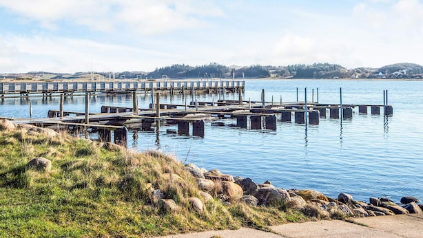 A waterfront dock with multiple piers extending into calm water, surrounded by grassy areas and distant hills. - 8 Person Holiday Home in Hojslev-by Traum (Hojslev)