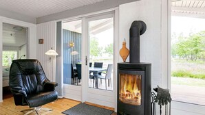 A cozy living room with a black leather chair, a wood-burning stove, and a view of the outdoors through large glass doors. - 8 Person Holiday Home in Hojslev-by Traum (Hojslev)