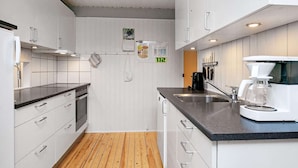 A modern kitchen with white cabinets, a wooden floor, a coffee maker, and a calendar on the wall. - 8 Person Holiday Home in Hojslev-by Traum (Hojslev)