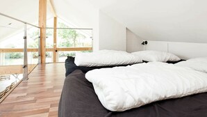 A modern bedroom with a large bed, a wooden floor, and a large window offering a view of the outdoors. - Luxurious Holiday Home in Falster by the Sea (Vaeggerlose)