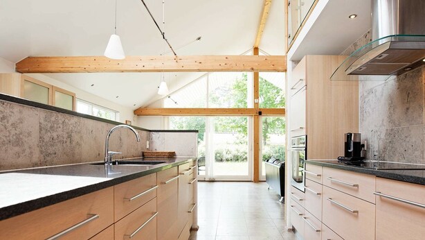 A modern kitchen with wooden beams, a large island with a sink, and a view to the outdoors. - Luxurious Holiday Home in Falster by the Sea (Vaeggerlose)