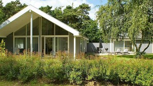 A modern house with a large glass extension, a patio with chairs, and a well-maintained lawn. - Luxurious Holiday Home in Falster by the Sea (Vaeggerlose)