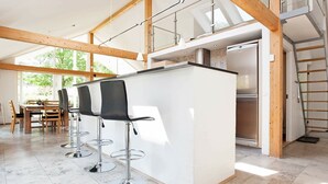 A modern kitchen with a central island, bar stools, and a dining area with a wooden table and chairs. - Luxurious Holiday Home in Falster by the Sea (Vaeggerlose)