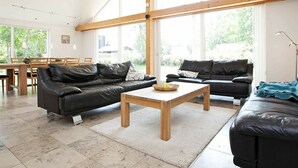 A spacious living area with two black leather sofas, a wooden coffee table, and a dining area with wooden furniture. - Luxurious Holiday Home in Falster by the Sea (Vaeggerlose)