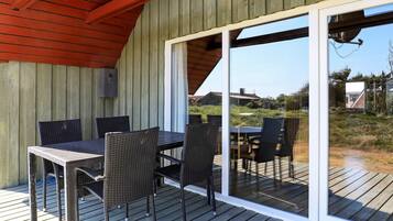 An outdoor deck with a table and chairs, a wooden ceiling, and a sliding glass door leading to a grassy area.