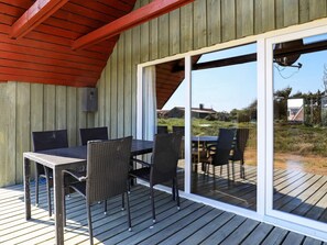 An outdoor deck with a table and chairs, a wooden ceiling, and a sliding glass door leading to a grassy area. - 6 Person Holiday Home in Hvide Sande (Hvide Sande)