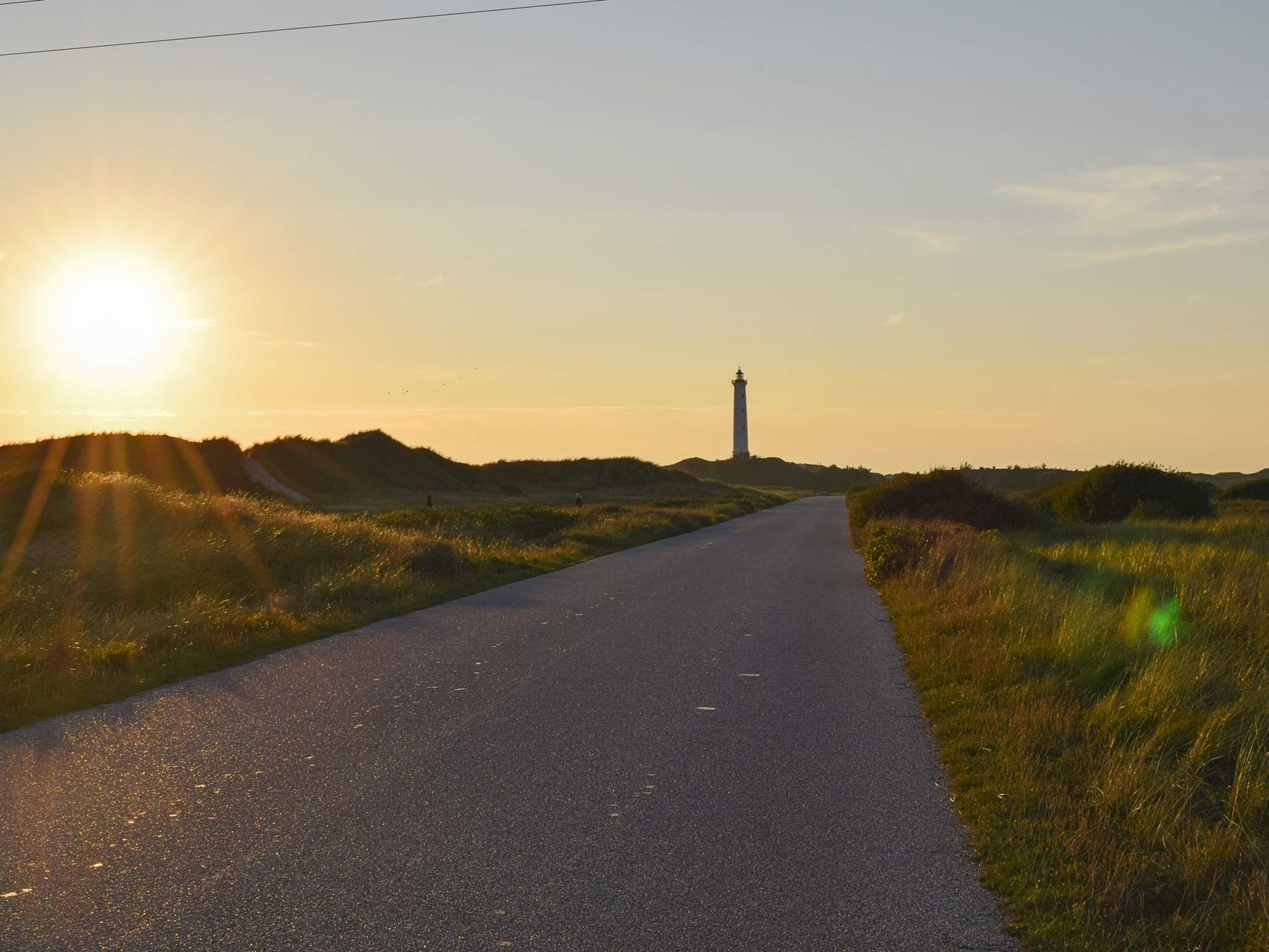 A road leading to a lighthouse with a clear sky and sun setting or rising.