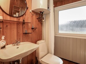 Une salle de bain avec des lambris en bois, un lavabo blanc, des toilettes, un miroir et une fenêtre donnant sur un paysage enneigé.
