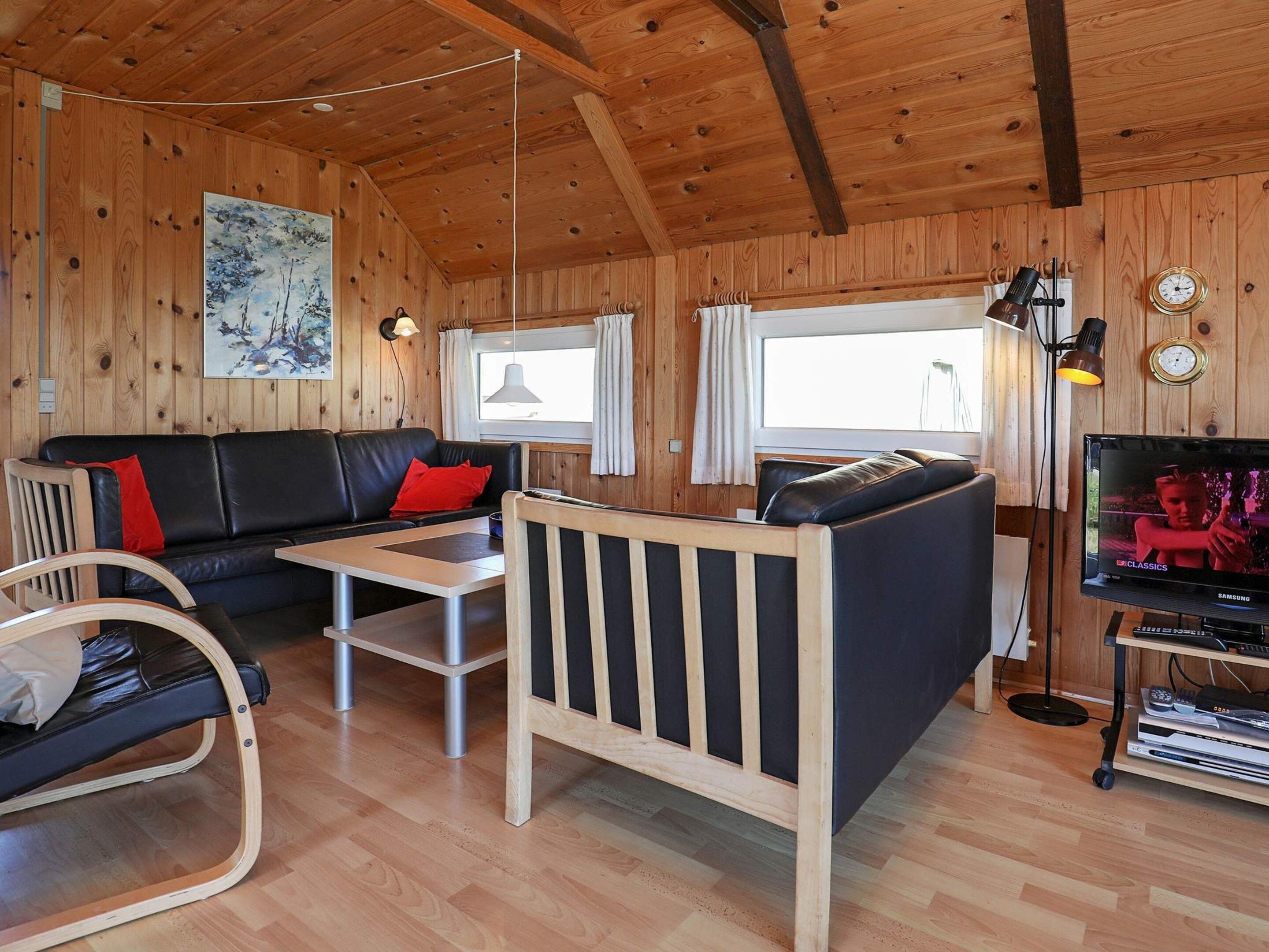 A cozy cabin interior with a wooden ceiling, a sofa, a dining table, a TV, and a bookshelf.