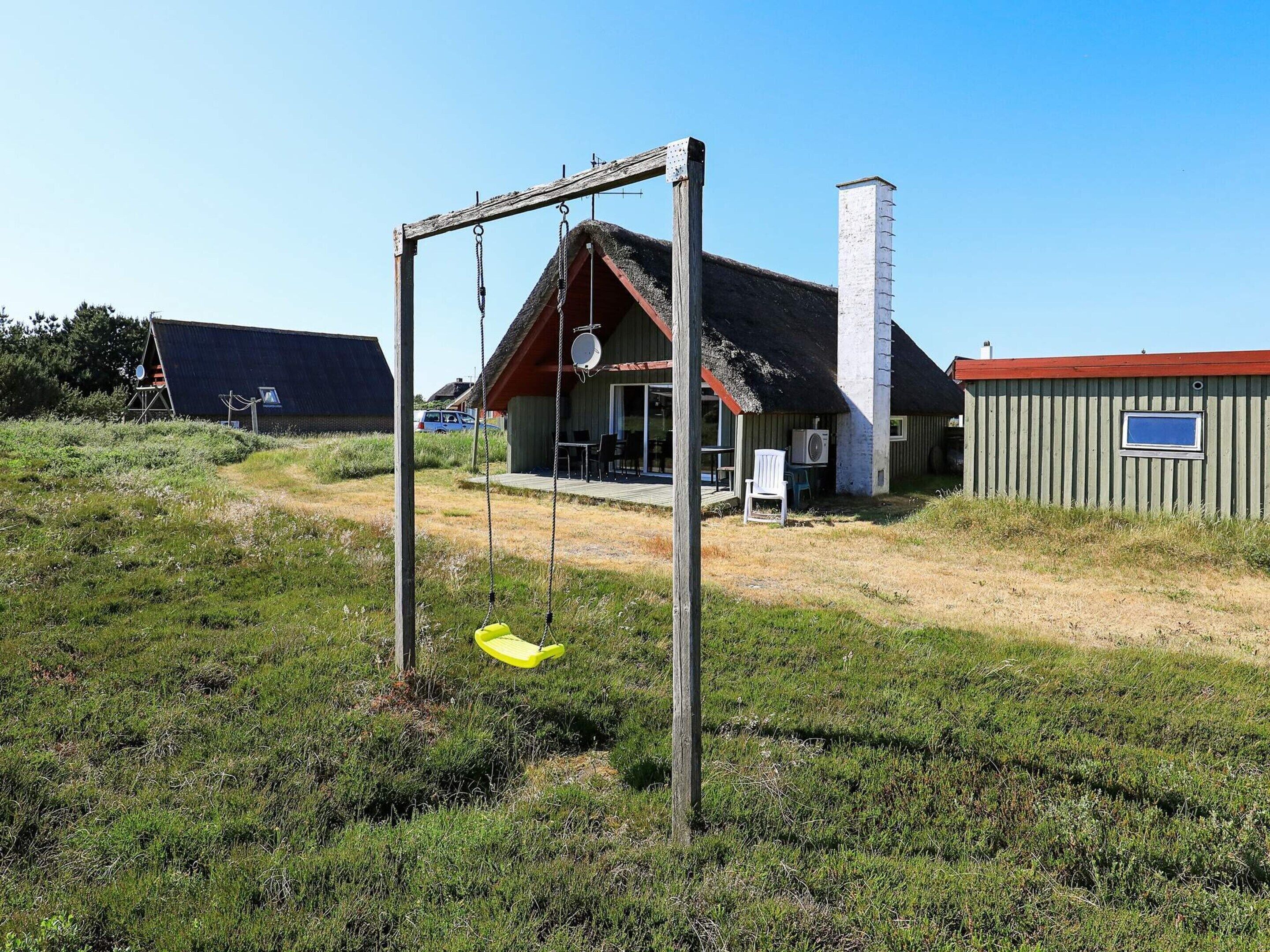 A rustic building with a thatched roof, a swing set, and a small outdoor seating area.