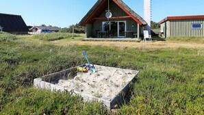 A thatched-roof building with a satellite dish, a tall white structure, and a fenced area with a shovel and toys. - 6 Person Holiday Home in Hvide Sande (Hvide Sande)