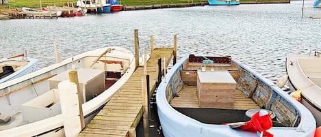 Un muelle con varias embarcaciones amarradas, un espigón de madera y un pequeño edificio al fondo.