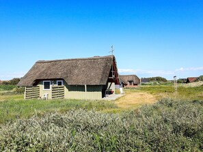 A traditional thatched-roof house with a wooden exterior, a small porch, and a chair outside.