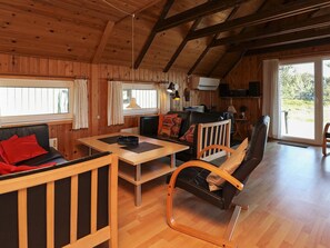 A wooden interior with a dining table, chairs, a sofa, and a television.
