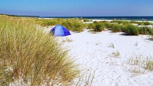 Une tente sur une plage de sable, avec de l’herbe au premier plan et l’océan en arrière-plan.
