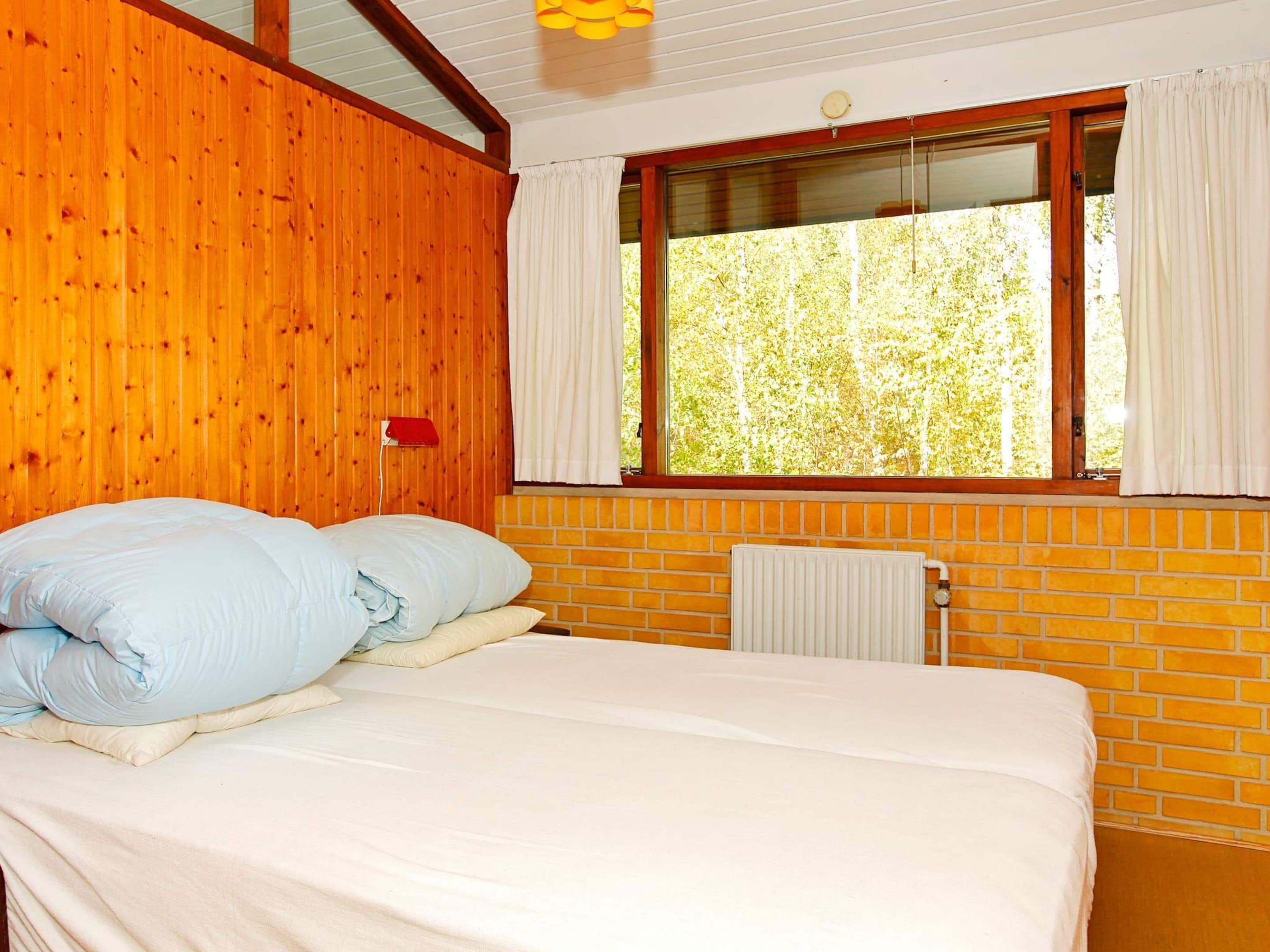 Una habitación con cama, ventana con cortinas, radiador y paredes de madera.