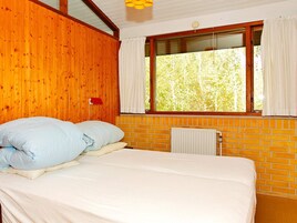 Una stanza con un letto, una finestra con tende, un termosifone e pareti in legno.