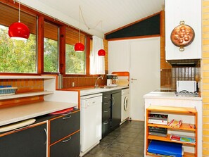 Eine Küche mit Geschirrspüler, Spüle und Kaffeemaschine. Rote Pendelleuchten und ein Kupfertopf sind an der Wand angebracht.