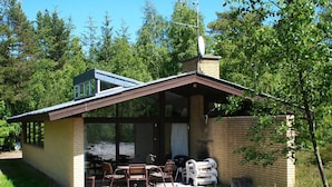 A small, single-story building with a sloped roof, large windows, and a patio area with outdoor furniture. - 4 Star Holiday Home in Nexo (Nexø)