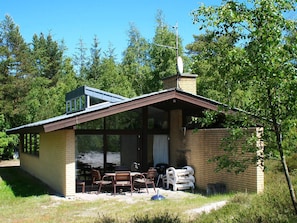 A small, single-story building with a sloped roof, large windows, and a patio area with outdoor furniture. - 4 Star Holiday Home in Nexo (Nexø)