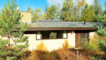 A single-story house with a sloped roof, surrounded by dense vegetation and trees.