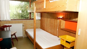 Habitación con literas, escritorio, silla, radiador y ventana con cortinas.