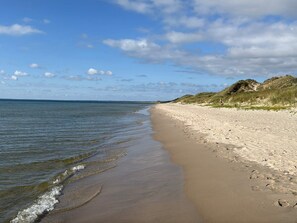 A sandy beach with gentle waves, a clear sky, and dunes in the background. - Elegant Holiday Home in Ålbæk near Sea (Aalbaek)