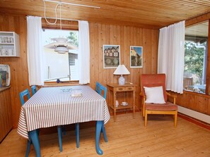 A wooden-paneled room with a dining table, chairs, a lamp, and a chair with a cushion.