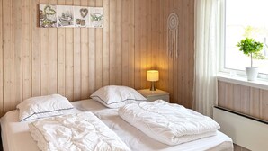 A double bed with white bedding, a bedside table with a lamp, and a wall with a dreamcatcher and artwork. - 4 Star Holiday Home in Vaeggerlose (Vaeggerlose)