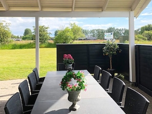 Eine überdachte Terrasse mit Esstisch, umgeben von Korbstühlen und einer Blumenvase auf dem Tisch.