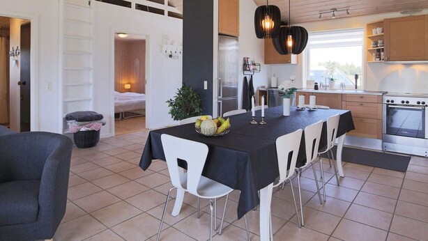 A modern kitchen with a dining area, featuring a black tablecloth, white chairs, and a central white vase with flowers. - 4 Star Holiday Home in Vaeggerlose (Vaeggerlose)