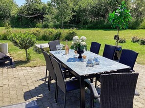An outdoor dining area with a table set for four, surrounded by wicker chairs. - 4 Star Holiday Home in Vaeggerlose (Vaeggerlose)