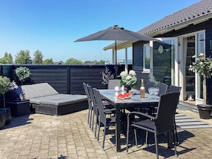 An outdoor patio with a table set for dining, surrounded by chairs, a large umbrella, and a sofa. - 4 Star Holiday Home in Vaeggerlose (Vaeggerlose)