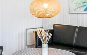 A round table with a white vase containing dried plants, a black leather sofa, and a woven lamp. - 4 Star Holiday Home in Jerup (Jerup)