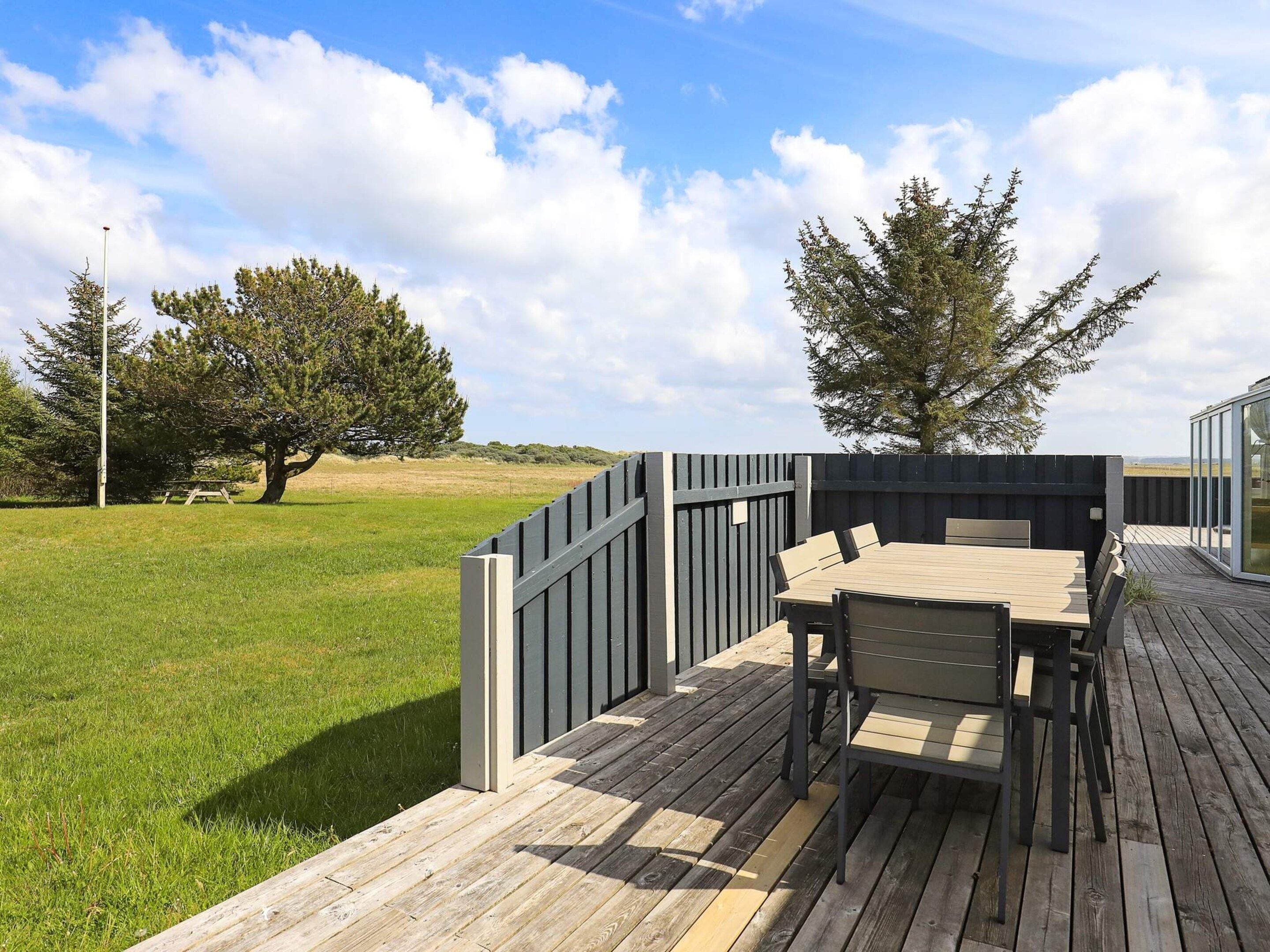 Een houten terras met een tafel en stoelen, omringd door een hek en bomen.