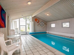 An indoor swimming pool with a tiled floor, white plastic chairs, and a ceiling with wooden panels. - 4 Star Holiday Home in Jerup (Jerup)