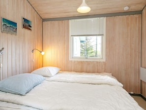 A bedroom with a bed, a bedside lamp, a window, and wooden walls.